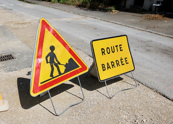 2 panneaux de signalisation, "Travaux" et "Route barrée", sur une voie en cours de réfection.